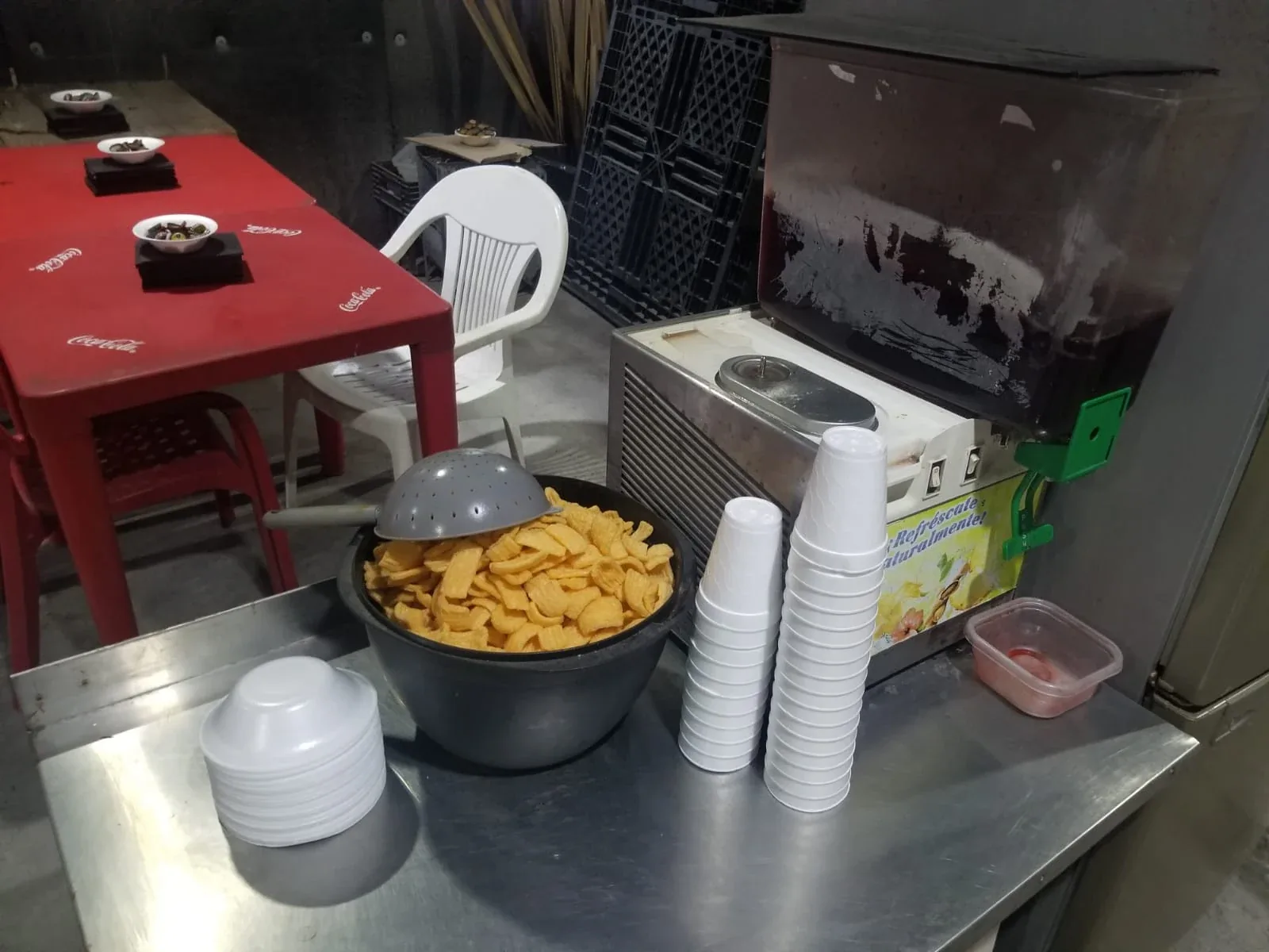 Mesa de botanas: chicharrones, vasos y dispensador de agua de jamaica
